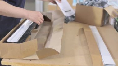 Plastik parçaları bir kutuya koymak. İşçi, müşteriye göndermek için malları bir kutuya koyar..