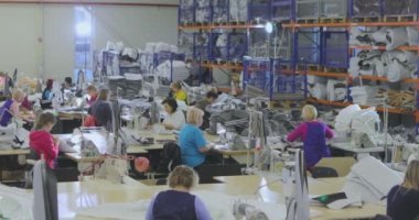 Birçok terzi bir giyim fabrikasında çalışır. Bir giyim fabrikasında çalışma süreci. Büyük dikiş atölyesi. Terziler fabrikada ürün yapar. Kumaş fabrikası.