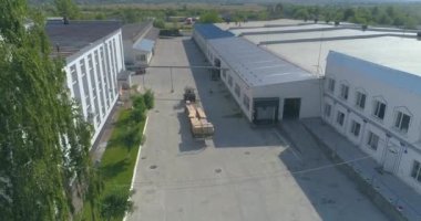 Traktör keresteleri fabrikanın arazisinden boş taşır. Traktör fabrikanın bölgesinden geçiyor. İnsansız hava aracından görüntüle.