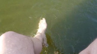 Mens feet in the water. A man dangles his feet in the river. A man swings his legs in the river.