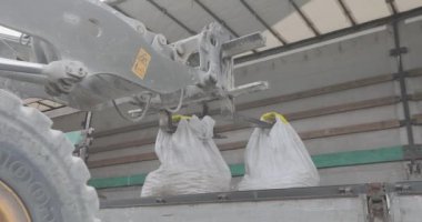 Bir buldozer çantaları bir kamyona boşaltır. Malları kamyondan boşaltıyorum. Buldozer arabadan mal indirir..