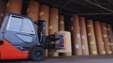 The forklift is carrying a large roll of paper. A forklift is carrying paper at the factory. Loader at the wallpaper factory.