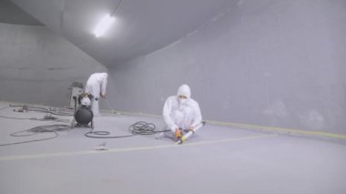 The builder smoothes the surface of the floor with a spatula. A builder in a protective suit creates a polymer floor.