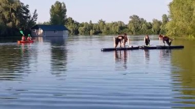 Girls do sports exercises on the sup board. Physical exercises on the sup board. Sports recreation on the river. Water sports.