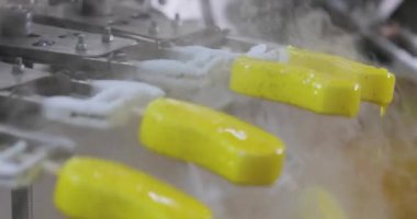 Ice cream is dipped into a container with fruit glaze. Colorful bright ice cream on the conveyor. Ice cream production.