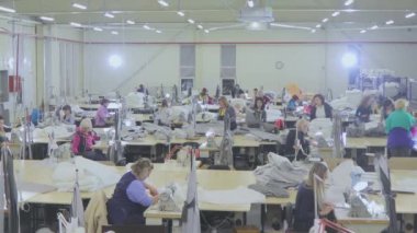 Birçok terzi bir giyim fabrikasında çalışır. Bir giyim fabrikasında çalışma süreci. Büyük dikiş atölyesi. Terziler fabrikada ürün yapar. Kumaş fabrikası.