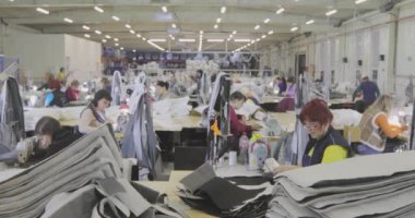 Birçok terzi bir giyim fabrikasında çalışır. Bir giyim fabrikasında çalışma süreci. Büyük dikiş atölyesi. Terziler fabrikada ürün yapar. Kumaş fabrikası.