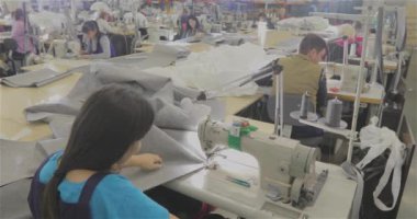 Birçok terzi bir giyim fabrikasında çalışır. Bir giyim fabrikasında çalışma süreci. Büyük dikiş atölyesi. Terziler fabrikada ürün yapar. Kumaş fabrikası.