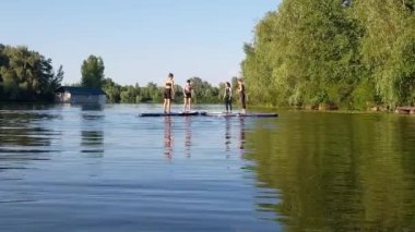 Girls do sports exercises on the sup board. Physical exercises on the sup board. Sports recreation on the river. Water sports.