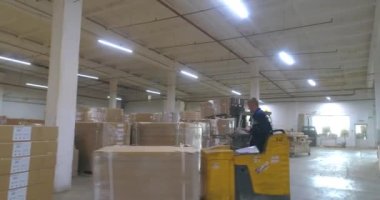 Fabrikada bitmiş ürünlerle dolu büyük bir depo. Fabrikada kutularla dolu bir depo. Büyük bir depodaki bir forklift kutuları taşır..