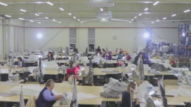 Birçok terzi bir giyim fabrikasında çalışır. Bir giyim fabrikasında çalışma süreci. Büyük dikiş atölyesi. Terziler fabrikada ürün yapar. Kumaş fabrikası.