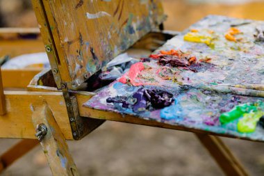 Güneşli bir sonbahar gününde bir manzara çizerken ressam renk paletiyle sığ alan derinliği (seçici odak) resmi.