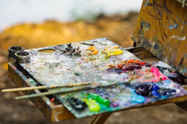 Güneşli bir sonbahar gününde bir manzara çizerken ressam renk paletiyle sığ alan derinliği (seçici odak) resmi.