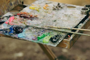 Güneşli bir sonbahar gününde bir manzara çizerken ressam renk paletiyle sığ alan derinliği (seçici odak) resmi.