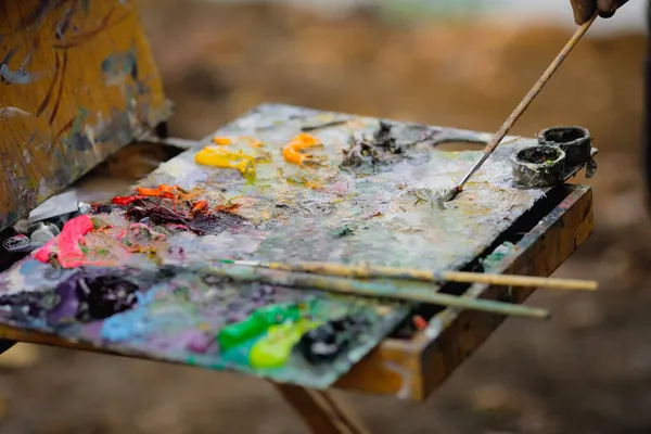 Güneşli bir sonbahar gününde bir manzara çizerken bir ressam ve renk paleti ile sığ alan derinliği (seçici odak) resmi.