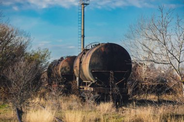 Güneşli bir kış gününde, bir tarlanın ortasında eski ve paslı demiryolu petrol tankerleriyle sığ alan derinliği (seçici odak) görüntüsü.