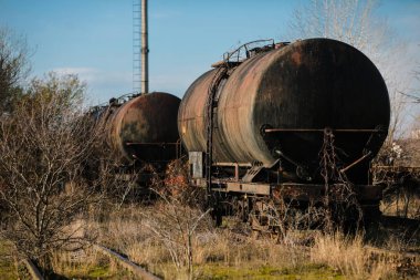 Güneşli bir kış gününde, bir tarlanın ortasında eski ve paslı demiryolu petrol tankerleriyle sığ alan derinliği (seçici odak) görüntüsü.
