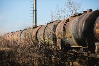 Güneşli bir kış gününde, bir tarlanın ortasında eski ve paslı demiryolu petrol tankerleriyle sığ alan derinliği (seçici odak) görüntüsü.