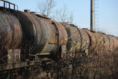 Güneşli bir kış gününde, bir tarlanın ortasında eski ve paslı demiryolu petrol tankerleriyle sığ alan derinliği (seçici odak) görüntüsü.
