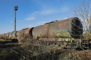 Güneşli bir kış gününde, bir tarlanın ortasında eski ve paslı demiryolu petrol tankerleriyle sığ alan derinliği (seçici odak) görüntüsü.