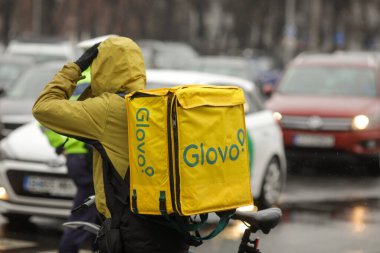 Bükreş, Romanya - 17 Aralık 2021: Bükreş sokaklarında Glovo teslimat çantası taşıyan adam.