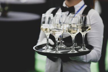 Saha derinliğinin derinliği (seçici odak) ayrıntıları bir garsonun etrafta dolanıp bir etkinliğin konuklarına şarap kadehleri sunmasıdır..