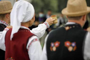 Braila, Romanya - 26 Ağustos 2021: Geleneksel Romen kıyafetleri giymiş erkek ve kadınlar geleneksel bir Romen erik brendisi olan tuica veya palinka dansı veya içiyorlar.