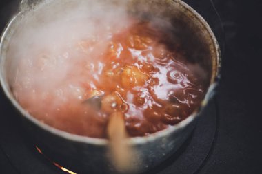 Romanya 'da kırsal bir evin arka bahçesindeki kırmızı tuğlalardan yapılmış yanan bir odun sobasının üzerine gulaş güveci kaynatan demir kazan dökün..