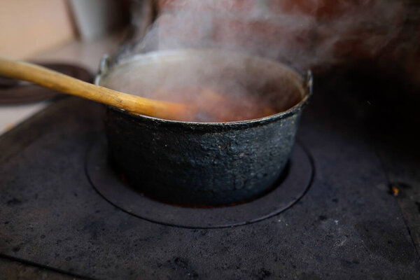 Cast iron cauldron boiling a goulash stew over a wood burning stove made from red bricks in the backyard of a rural house in Romania.