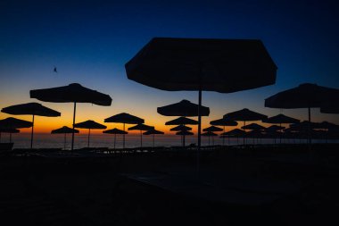 Güneş şemsiyeleri güneş doğmadan hemen önce Bulgaristan 'ın Obzor tatil beldesindeki Karadeniz' de sakin ve sıcak bir yaz sabahında sahilde görülüyor..