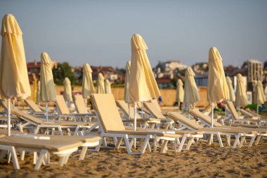 Bulgaristan 'ın Obzor tatil beldesindeki Karadeniz' de sakin ve sıcak bir yaz sabahında plajda şezlonglar ve güneş şemsiyeleri.
