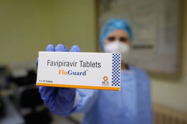 Bükreş, Romanya - 24 Ocak 2022: Bir kutu Favipiravir antiviral ilaç taşıyan bir sağlık çalışanının sığ alan derinliği (seçici odak) ayrıntıları.