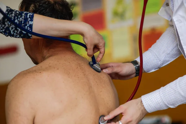 Bir doktor ve bir kadın doktor erkek bir hastanın sağlığını kontrol eder..