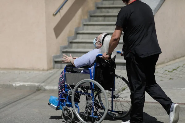 罗马尼亚布加勒斯特 2022年5月9日 一名有秩序的男子将一名坐在轮椅上的老年男性病人推倒在一家罗马尼亚医院的水泥地上 — 图库照片