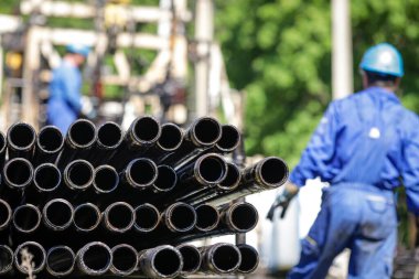 Oil rig drill pipes stacked with oil industry workers in the background. Oil and gas industry. Crude oil pump jack on an oil field. Drilling of oil and gas wells.