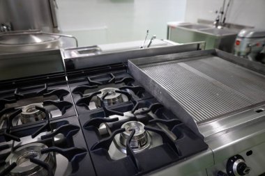 Shallow depth of field (selective focus) details with a brand new, unused, professional metallic gas burner in a restaurant kitchen.