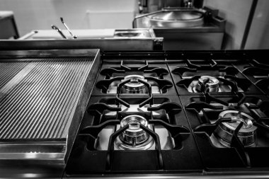 Black and white shallow depth of field (selective focus) details with a brand new, unused, professional metallic gas burner in a restaurant kitchen.