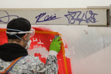 Bucharest, Romania - September 3, 2022: Details with the hand of a young man, with protective gloves and goggles, scraping off the graffiti from a glass wall.