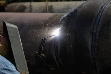 Shallow depth of field (selective focus) details with a professional welder welding an industrial metallic pipeline.