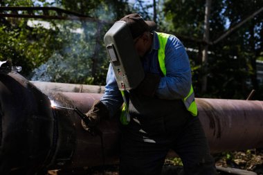 Shallow depth of field (selective focus) details with a professional welder welding an industrial metallic pipeline.