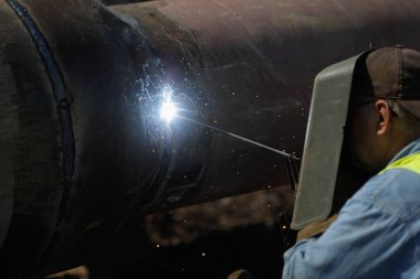 Shallow depth of field (selective focus) details with a professional welder welding an industrial metallic pipeline.