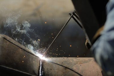 Shallow depth of field (selective focus) details with a professional welder welding an industrial metallic pipeline.