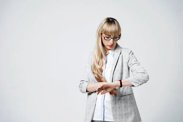 Giovane bella donna bionda in studio su sfondo grigio chiaro. Modello in pantalone e occhiali tempo di controllo con orologio da polso. — Foto Stock
