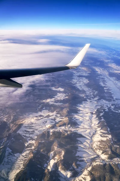 Voar e viajar. Vista da janela do avião na asa durante o pôr do sol. Avião sobre montanhas no inverno. — Fotografia de Stock