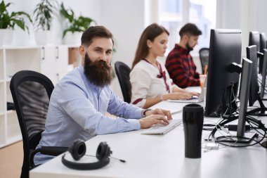 Modern bilişim ofisinde çalışan insanlar. Bir grup genç programcı ve yazılım geliştirici bilgisayar üzerinde çalışan masalarda oturuyorlar. Ekip iş başında.