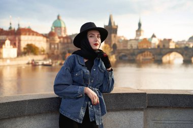 Prag 'da siyah şapka takan zarif genç bir kadın ve arkasında Charles Bridge var. Zarif retro bayan güzel sanat portresi.