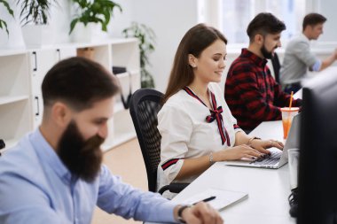 Modern bilişim ofisinde çalışan insanlar. Bir grup genç programcı ve yazılım geliştirici bilgisayar üzerinde çalışan masalarda oturuyorlar. Ekip iş başında.