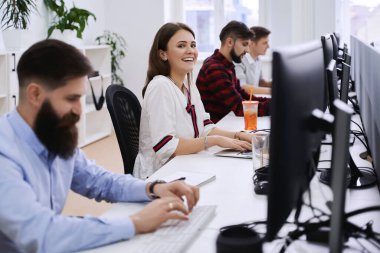 Modern bilişim ofisinde çalışan insanlar. Bir grup genç programcı ve yazılım geliştirici bilgisayar üzerinde çalışan masalarda oturuyorlar. Ekip iş başında.