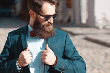 Stylish man with beard wearing a jacket, shirt and bow tie on a sunny day