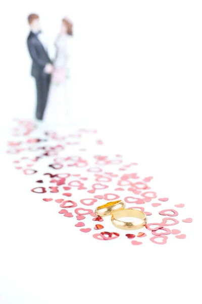 Pure gold wedding rings with red hearts ornament and porcelain bride and groom background — Stock Photo, Image